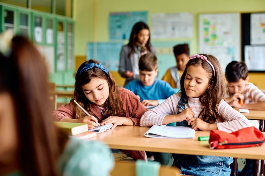 Happy elementary school classmates taking a test in the classroom.